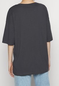 Tmavě šedé oversized tričko s krátkými rukávy, kulatým výstřihem a hladkým povrchem. Viditelné švy podél lemů a švů.