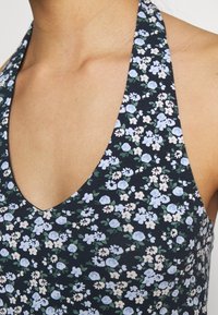 Blommig halterneck-topp i mörk marinblå med små blå och vita blommor. Har en djup V-ringning och mjukt, texturerat tyg.