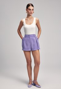 Shorts violets taille haute avec poches avant, associés à un débardeur blanc côtelé et des chaussures à talons lilas avec une boucle décorative.