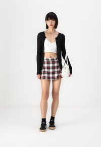 Czarny kardigan z długim rękawem na białej bluzce crop top; mini spódnica w czerwoną i czarną kratę; biała torebka na ramię; czarne sneakersy z jasnymi podeszwami.