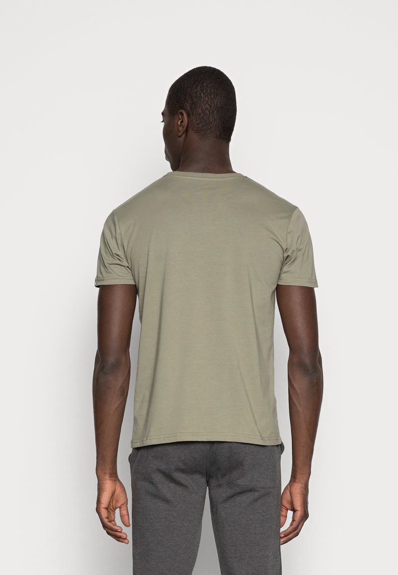 Camiseta de algodón suave en color verde oliva con mangas cortas. Presenta un clásico escote redondo y dobladillo recto, combinada con pantalones gris oscuro.