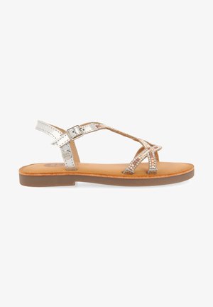 Sandali metallici argento con cinturini incrociati, caratterizzati da dettagli in strass e una soletta in pelle beige. Suola piatta con chiusura a fibbia.