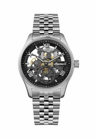 Srebrny skeletonowy zegarek z czarną tarczą, przezroczystymi mechanizmami i rzymskimi cyframi jako znacznikami godzin. Metalowa bransoleta o wykończeniu polerowanym.