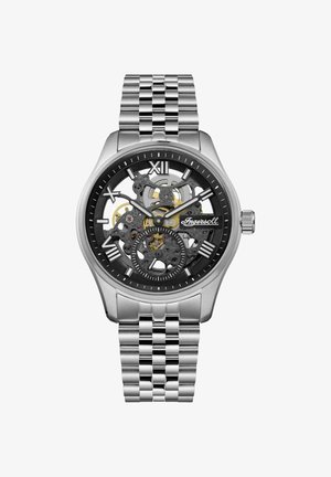 Montre squelette argentée avec un cadran noir, mécanique transparente et chiffres romains pour les heures. Fin de bracelet en métal avec une texture polie.