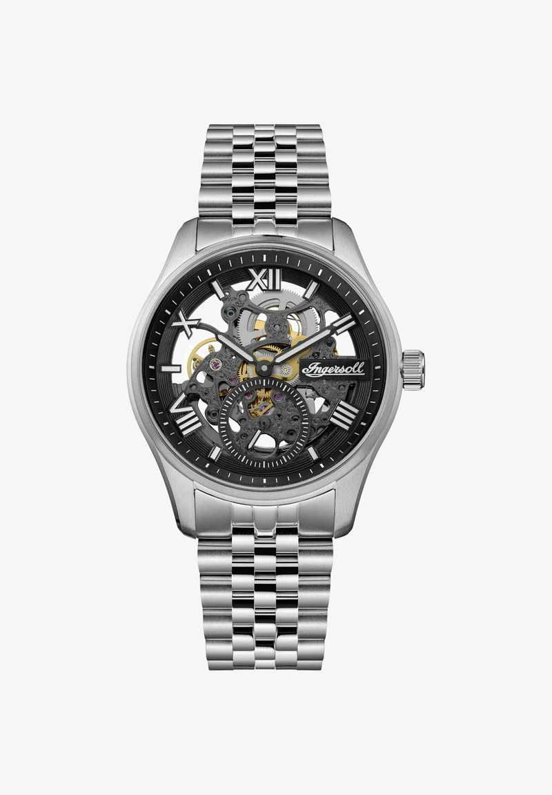 Srebrny skeletonowy zegarek z czarną tarczą, przezroczystymi mechanizmami i rzymskimi cyframi jako znacznikami godzin. Metalowa bransoleta o wykończeniu polerowanym.