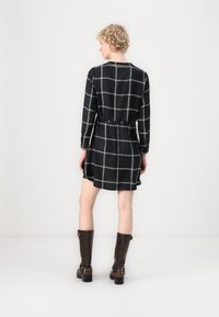 Rochie cu carouri negre, cu mâneci lungi, talie cu brâu și tiv evazat, asortată cu cizme maro din piele până la genunchi.