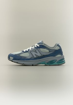 Lyseblå og grå New Balance løbesko med hvide snørebånd og blågrønne detaljer på sålen, vist i profil.