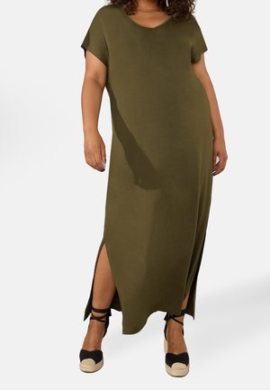 Nainen pukeutunut oliivinvihreään, lyhythihainen maksimekkoon, jossa on sivuhalkiot, ja mustiin espadrillakiilakorkoihin, joissa on nilkkahihnat.