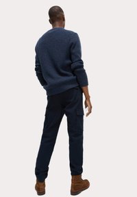 Marine gebreid sweater met geribbelde halslijn en manchetten, gecombineerd met donkere sweatpants met zijzakken en bruine suède enkellaarzen.
