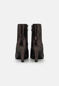 Bottes de cheville noires à talons avec une finition texturée, présentant une fermeture éclair sur le côté et un talon effilé. Le design est élégant avec une esthétique minimaliste.