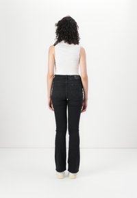 Svarte utsvingte jeans med høy midje og fem lommer, parret med en tettsittende hvit ermeløs topp, sett fra baksiden.
