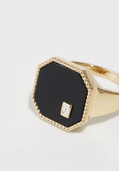 Gold ring with an octagonal black stone, featuring a small rectangular clear gemstone. Edges have a twisted rope design for texture.
