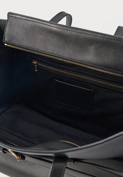 Εσωτερικό μαύρης δερμάτινης τσάντας χειρός με τσεπάκι με φερμουάρ, επένδυση από ύφασμα και διπλές κορυφαίες λαβές με χρυσούς μεταλλικούς εξαρτηματάκια.