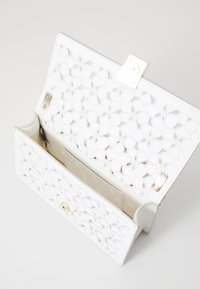 Borsa bianca con motivo floreale intagliato, dettagli in hardware dorato e interno foderato. Chiusura a scatto in cima.