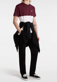 T-shirt a righe bordeaux e bianche con logo, indossato con pantaloni jogger neri e sneakers Vans nere. Felpa legata in vita.