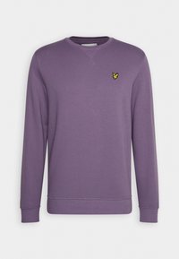 Sudadera púrpura con cuello redondo, mangas largas y puños acanalados. Presenta un pequeño logotipo amarillo en el lado izquierdo del pecho. Textura suave.