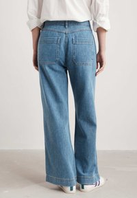 Jeans a gamba larga azzurro chiaro in denim, con vita alta, due tasche posteriori e dettagli di cucitura discreti. Indossati con sneakers bianche.