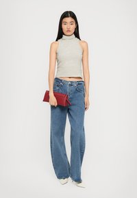 Top senza maniche grigio e bianco a righe, con scollo alto, abbinato a jeans blu larghi e una pochette rossa. Scarpe bianche con punta affilata.