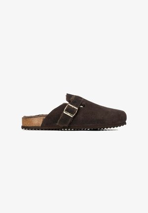 Zueco marrón oscuro tipo slip-on con empeine de ante, correa ajustable con hebilla, suela de corcho y forro interior peludo.