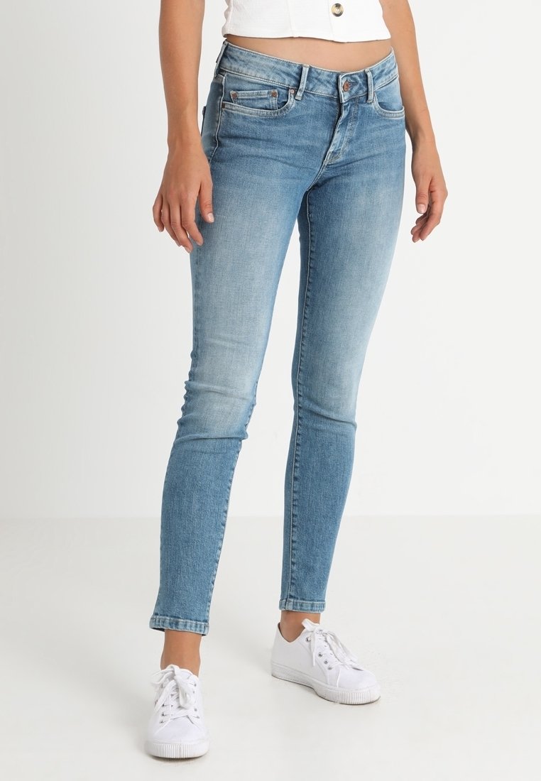 Jeans skinny de denim azul claro con acabado desgastado, diseño de cinco bolsillos y sutiles detalles de costura. Combinados con zapatillas blancas.