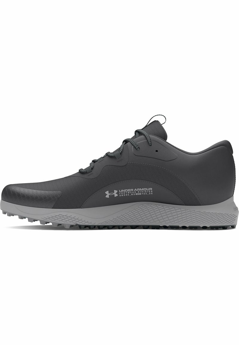 Zapato deportivo gris con un diseño texturizado, suela de goma con tacos de tracción y cordones elásticos para un ajuste seguro. Logo de Under Armour visible.