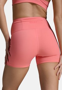 Shorts de sport roses avec une taille haute, fabriqués à partir d'un matériau extensible, dotés d'une texture lisse et d'un détail de logo subtil à l'arrière.