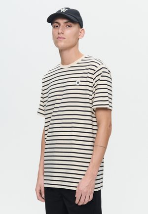 Beige and black striped t-shirt with short sleeves, round neck, and small logo on the left chest. Paired with a black cap.