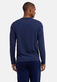 Marineblaues Langarmshirt aus weichem Stoff mit Rundhalsausschnitt. Hat eine lockere Passform und dezente Nähte. Kombiniert mit passenden Hosen.