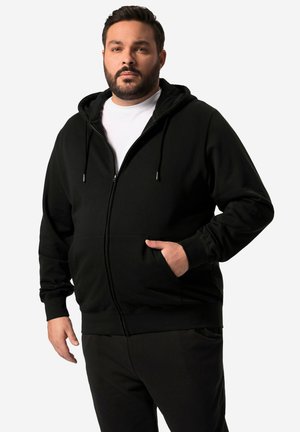 Schwarze Zip-Hoodie mit einer Fronttasche, Kordelzugkapuze und gerippten Bündchen. Über einem weißen T-Shirt getragen, das eine glatte Textur aufweist.