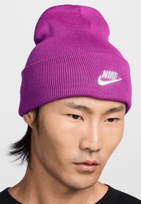 Beanie viola a maglia con una texture rigata e un bordo arrotolato, caratterizzato da un logo Nike bianco cucito sulla parte anteriore.