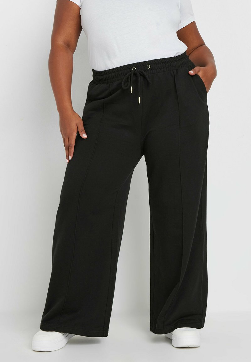 Svarta vida sweatpants med dragsko i midjan, sidofickor och mjuk tygkvalitet, kombinerat med vita sneakers.