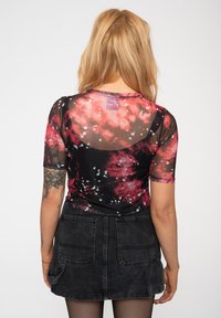 Black sheer top with red and white splatter pattern, short sleeves, round neckline; paired with a black denim skirt featuring pockets.