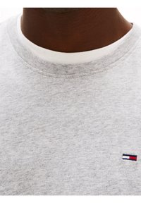 Gray sweatshirt with a round neckline, made from soft fabric. Features a small logo in red, white, and blue on the left chest area.
