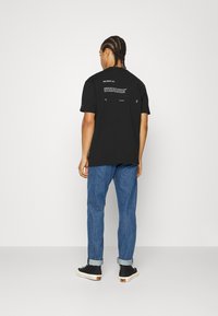 Svart t-skjorte med korte ermer med grafisk tekst og Puma-logo. Kombinert med rullede blå jeans og svarte sneakers.