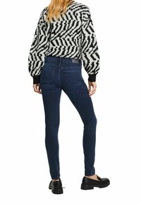 Jersey de manga larga con patrón en blanco y negro y mangas abullonadas, combinado con vaqueros pitillo azul oscuro y mocasines negros.