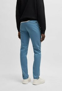 Pantalons en coton bleu chino avec une coupe slim. Dotés d'une poche arrière avec une étiquette logo discrète. Associés à un sweat-shirt noir et des baskets blanches.
