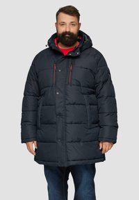 Dunkelblauer Puffermantel mit Kapuze, ausgestattet mit einem gesteppten Design, zwei Reißverschlusstaschen auf der Brust mit roten Akzenten und einem Knopfverschluss.