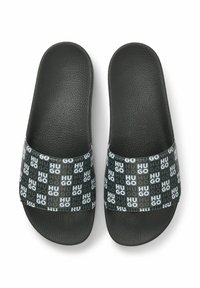 Czarne sandały wsuwane z fakturowaną górą z sztucznej skóry. Posiadają pleciony pasek z powtarzającym się logo „Hugo” w szaro-białych kolorach. Płaska podeszwa.