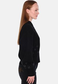 Svart stickad tröja med hög krage, med en texturerad yta och subtilt logomönster. Mjuk tyg och kort passform betonar formen.