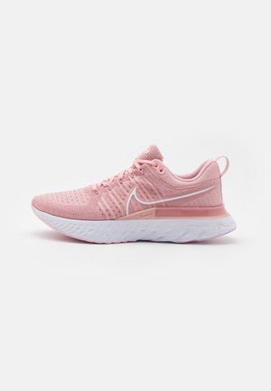 Chaussure de course Nike rose clair avec semelle blanche, empeigne en mesh, lacets et logo swoosh sur le côté, présentée de profil sur fond blanc.