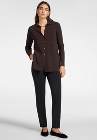 Donkerbruine lange mouwen knoopshirt met een kraag en een gebogen zoom. Gepaard met zwarte slim-fit broek en zwarte flats.