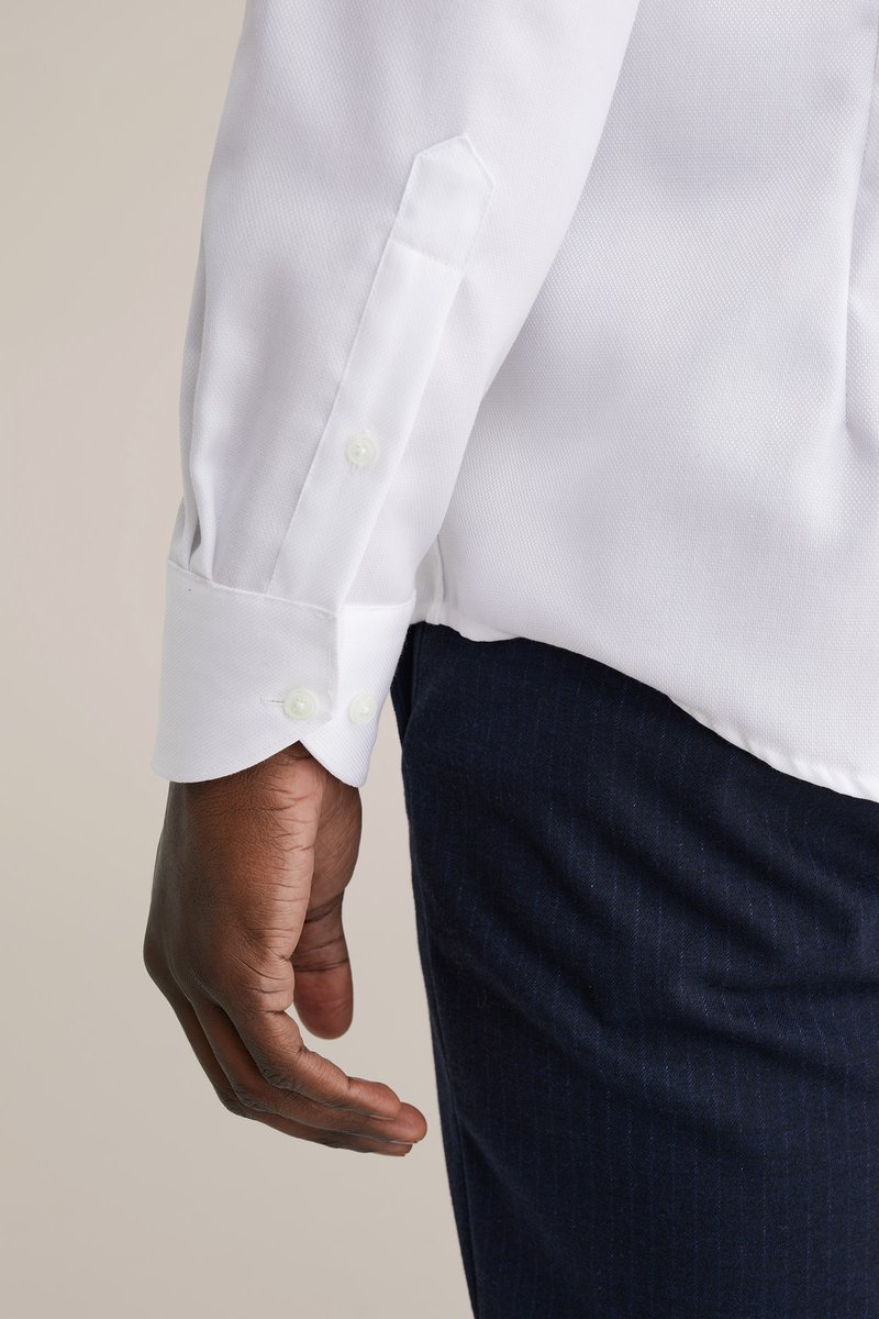 Witte langarmige blouse met een gestructureerde stof, knoopmanchetten en een schuin afgesneden mouwzoom, gecombineerd met donkerblauwe broek.