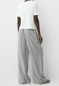 Vit, kortärmad skjorta med rundad halsringning, kombinerad med grå, vida randiga byxor. Tyget verkar lätt och har en mjuk textur.