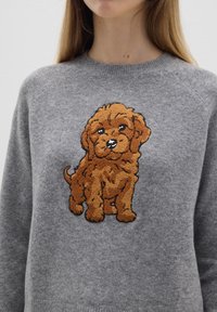 Grauer Pullover mit einem großen, strukturierten, braun gestickten Welpen auf der Vorderseite, mit rundem Halsausschnitt und Raglanärmeln.