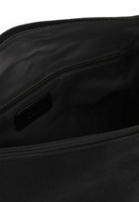 Intérieur d'un sac en tissu noir avec une poche zippée, présentant une texture lisse, des détails de couture et une étiquette de marque rectangulaire.