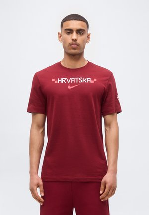Homme debout face à l'avant portant un t-shirt bordeaux avec "HRVATSKA" et un logo Nike sur la poitrine.