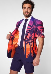 Spalvingas švarkas su gradientu nuo violetinės iki oranžinės, papuoštas palmės medžių grafika; derinamas su tamsiai mėlynomis šortais ir balta marškinėliais.