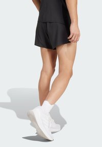 Shorts de sport noirs avec un design perforé, associés à des baskets blanches et des chaussettes chevilles. Les shorts présentent une coupe décontractée et un tissu léger.