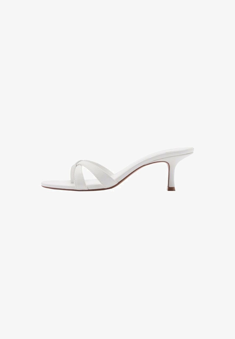 Mule blanche à bout ouvert avec des brides croisées et un talon fin de hauteur moyenne, montrée de profil sur fond blanc.