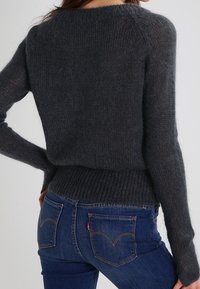 Pull gris foncé en maille avec un col rond, un ourlet côtelé et des manches longues, associé à un jean en denim bleu montrant le design des poches arrière.